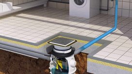 Im Bild ist eine Abwasserpumpe zu sehen, die in einem gefliesten Raum mit Waschmaschine und Rohrleitungen eingebaut ist.