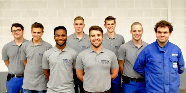 Die Männer zeigen eine freundliche Atmosphäre, während sie in zwei Reihen aufgestellt sind, einige mit Brillen und unterschiedliche Frisuren.