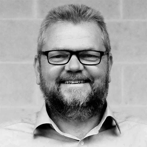 Der Mann zeigt ein freundliches Lächeln, während er in die Kamera schaut, umgeben von einer neutralen Hintergrundfarbe.