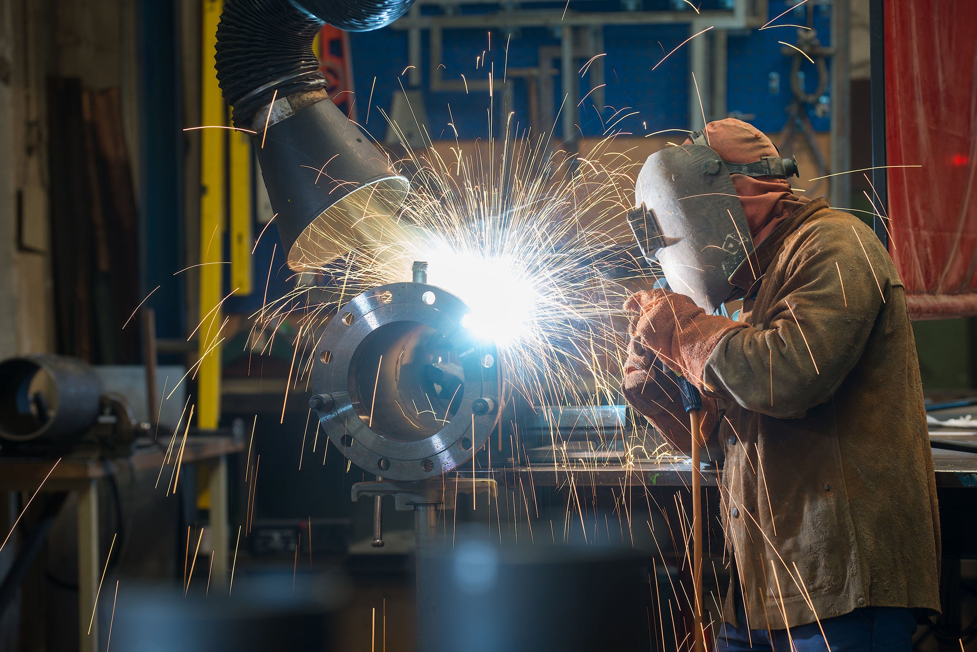 Ein Mann in Schweißermaske und Handschuhen führt präzise Schweißarbeiten durch, während ein intensives Licht und Funken sprühen.