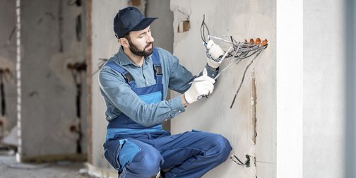 Ein Elektroniker der auf einem Rohbau die Kabel aus der Wand zieht