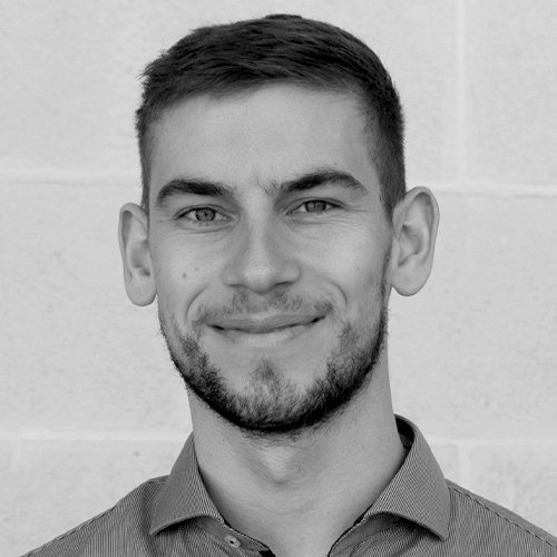 Der Mann trägt ein Hemd und hat kurzes, ordentlich frisiertes Haar, während er direkt in die Kamera schaut.