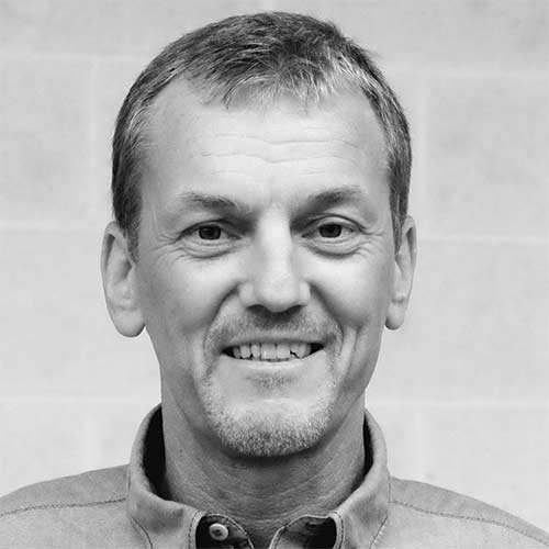 Der Mann trägt ein helles Hemd und hat einen freundlichen Gesichtsausdruck, der Wärme und Offenheit ausstrahlt.