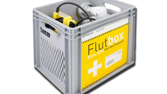 Eine graue Kiste mit gelbem Aufkleber, die als Flutbox für Erste Hilfe bei Hochwasser dient, steht auf einem weißen Hintergrund.